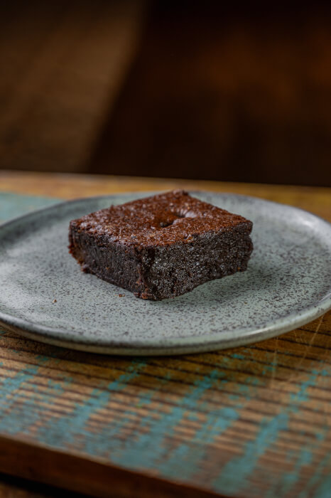 Brownie quadrado denso com açúcar cristalizado por cima, sobre prato de cerâmica artesanal